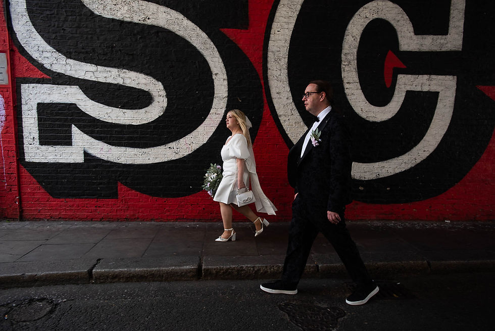 bride and groom walk along road beside colourful graffitti civered wall