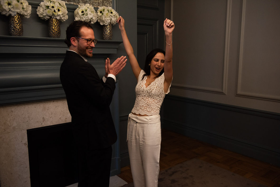Bride with arms in air whooping as groom claps.