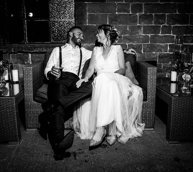 Relaxed couple seated together the brides hand on his lap he holds a pint laughing together