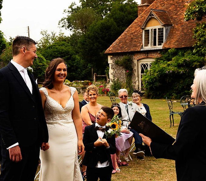 Documentary style wedding photo of couple standing at Nurstead Court outdoor alter with their small child looking up pulling a funny face at the vows.
