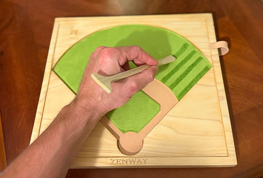 Hand using a wooden groundskeeing tool to create mowing stripes on Zenway Home Field, a handcrafted baseball zen garden.