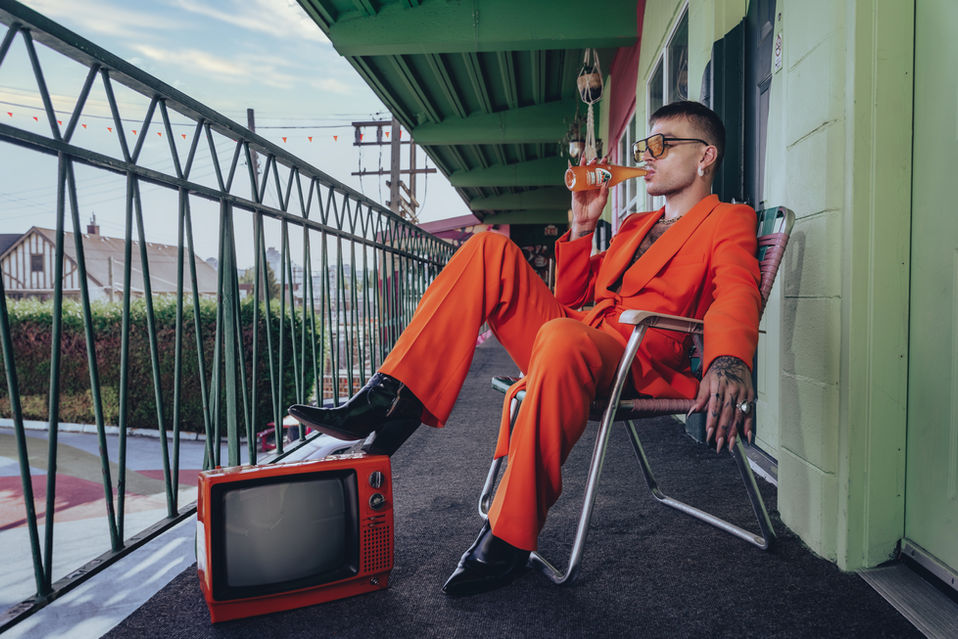 Male model in orange suit drinking an orange soda outside a motel