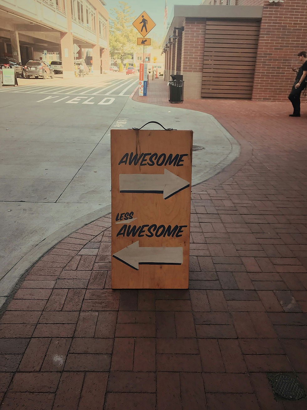 A sign showing an arrow to the left, labeled "awesome", and one to the right, labeled "less awesome". Symbolic of feedback for inclusive work culture.