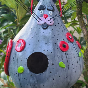 A gourd painted grey with red accents to resemble a cat. The cat is has a bow in its hair. The Cat/Gourd is a birdhouse