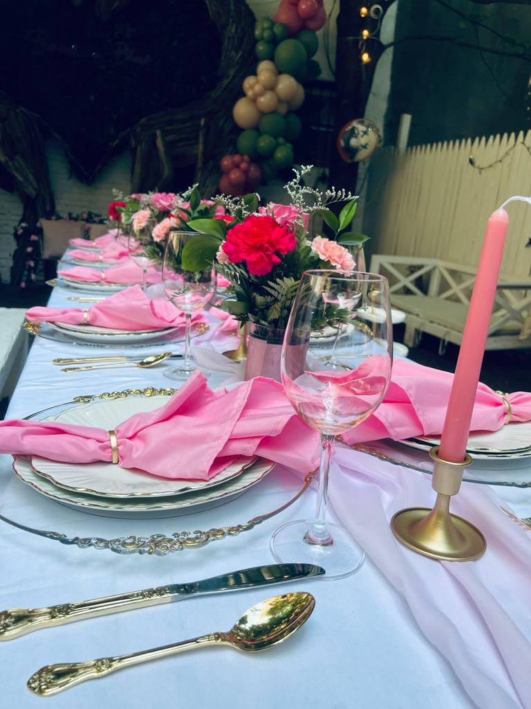 a table set for a party with pink napkins and candles