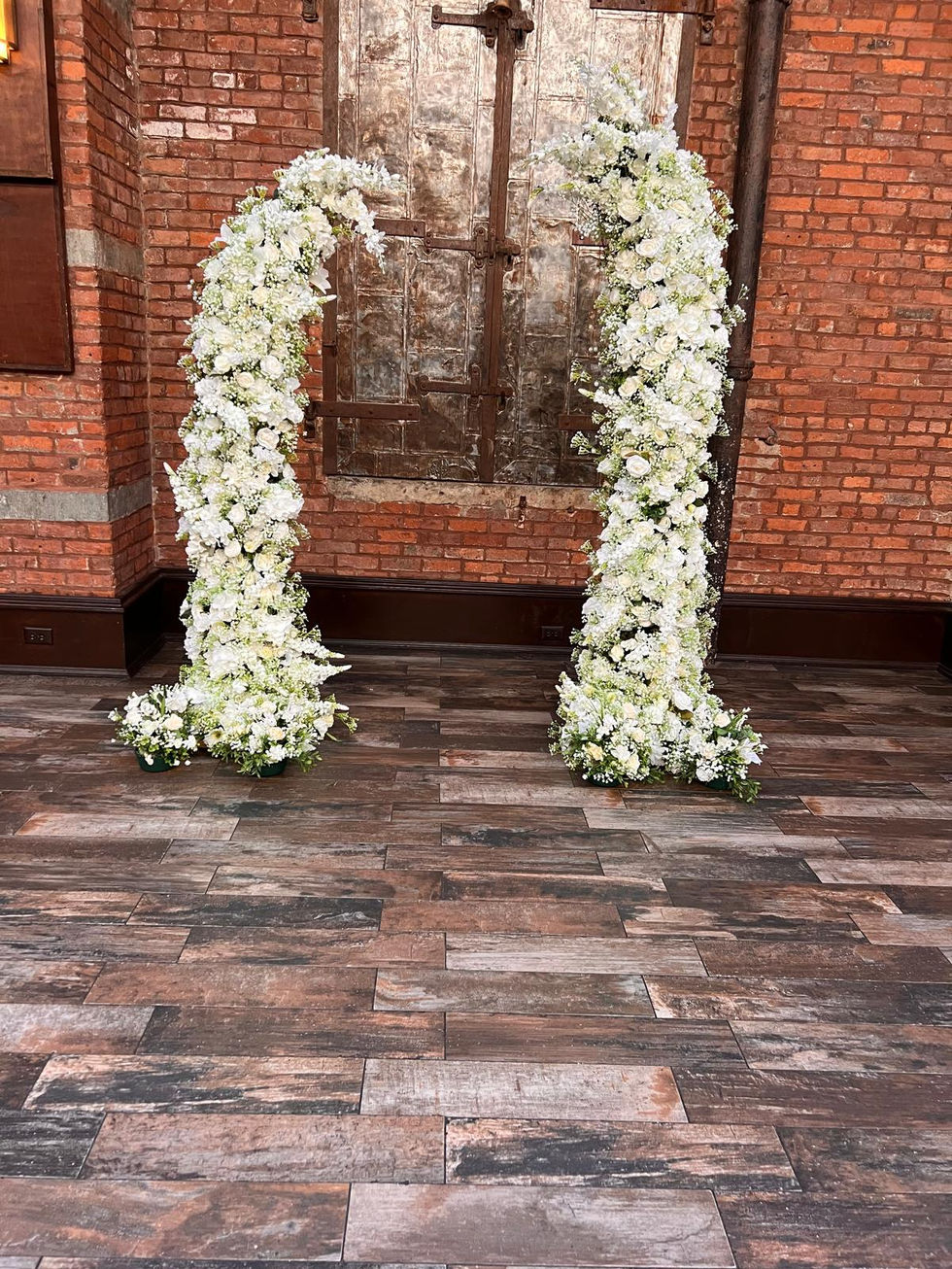 a large arch made of white flowers is sitting on a wooden floor in front of a brick wall .