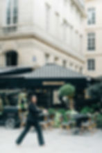 A person walking in front of an outdoor café in Pairs with black awning and tables, in a city with beige buildings could be the perfect inspiration for your next project on website or logo design in Edmonton and Calgary AB.