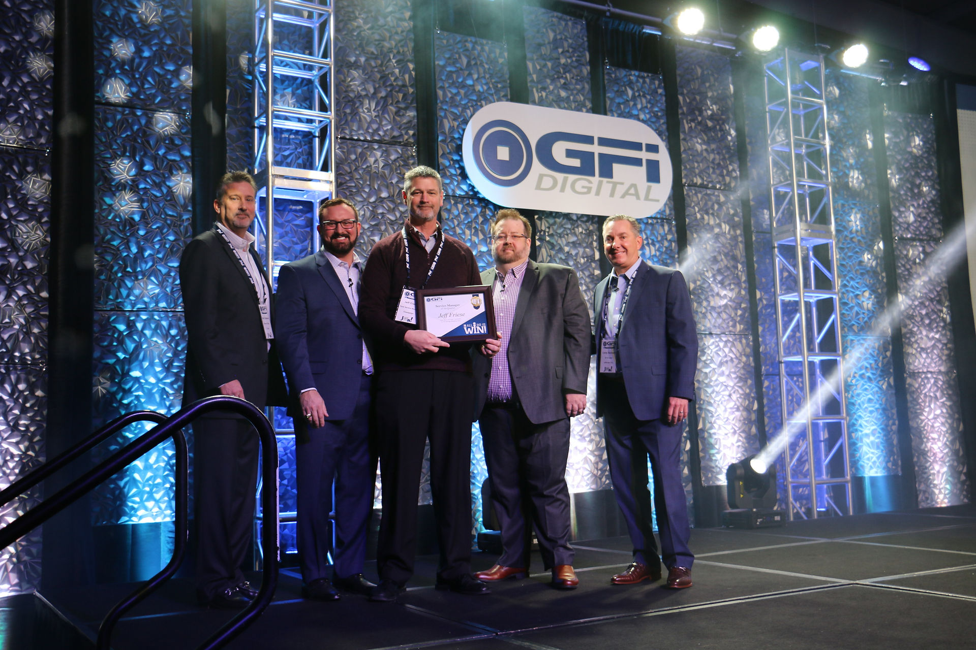 Group of men with award at GFI annual event in front of stage