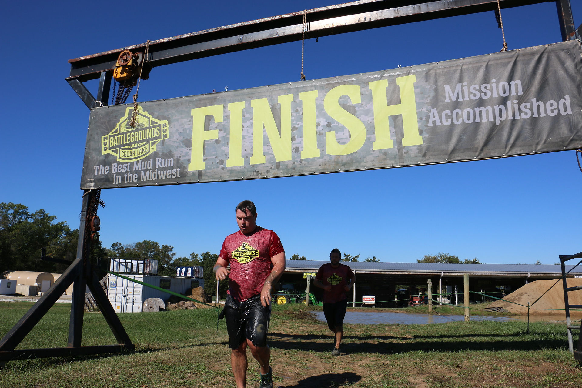 Two men running towards the finish line banner under the blue sky