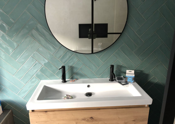 Moderne badkamer met wit wastafelmeubel, ronde spiegel en zwarte wandkraan.