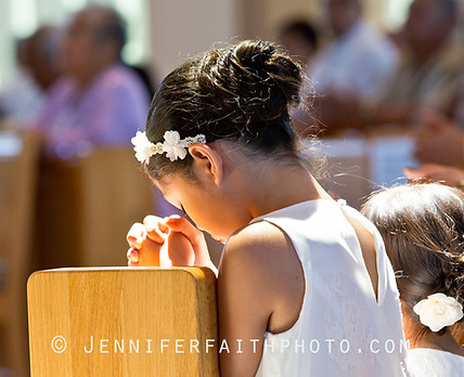 Young flower girl praying during Catholic wedding service.