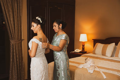 Bride getting help with dress by woman in room with bed and lamp