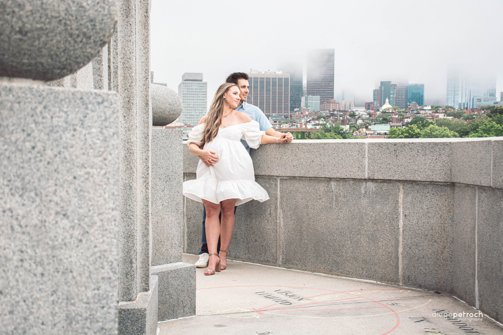 Couple embraces on a rooftop overlooking a city skyline on a cloudy day.