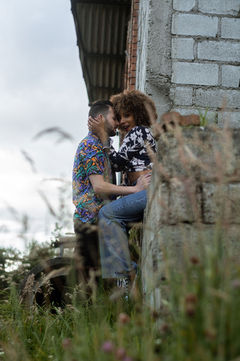 Couple embracing each other, sitting on a wall near a weathered building outside.