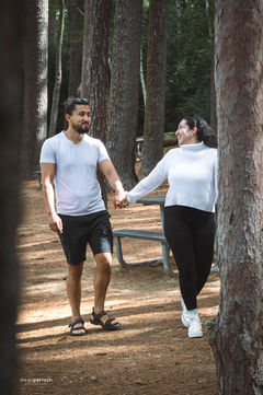 Couple holding hands in a park, smiling at each other. Yuliana + Fabio.