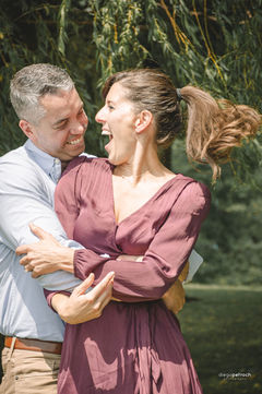 Smiling couple in embrace, woman laughing in a candid outdoor photo.