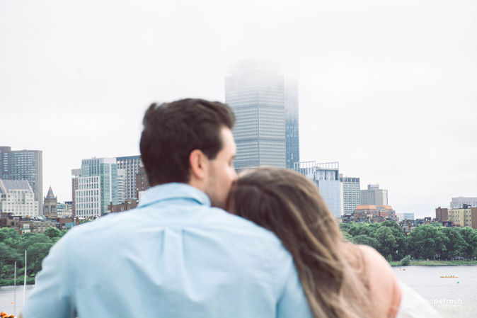 Couple embraces each other looking at city skyline with water by Caroline and Chandler.