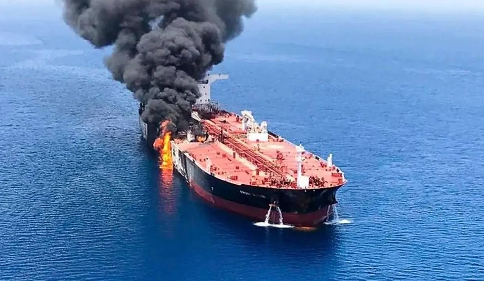 Large tanker ship burning at sea, with thick black smoke and flames rising from the deck over calm blue water.