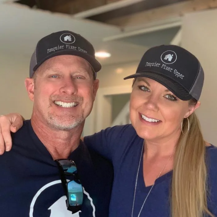 John and Kelly of Fauquier Fixer Upper, smiling in matching Fauquier Fixer Upper caps inside a house they're renovating