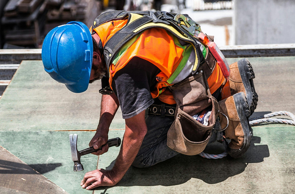 Roof worker in safety gear hammering shingles to the roof
