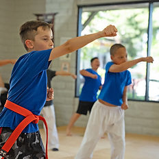 students in a martial arts class punching inthe air. All wearing blue shirts.