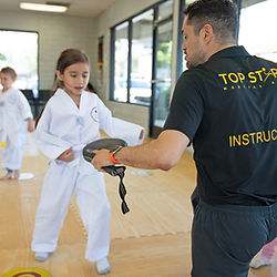Instructor holds taekwondo paddle for female child kicking - Premier Martial Arts