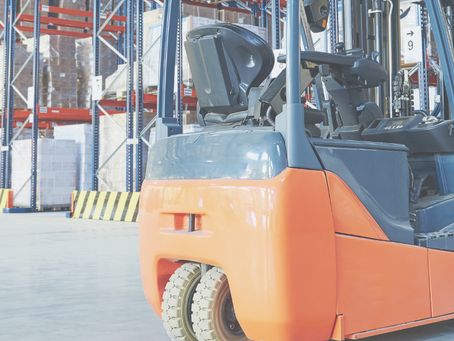 Manual hydraulic stacker beside an electric pedestrian stacker in a warehouse aisle with pallet racking.