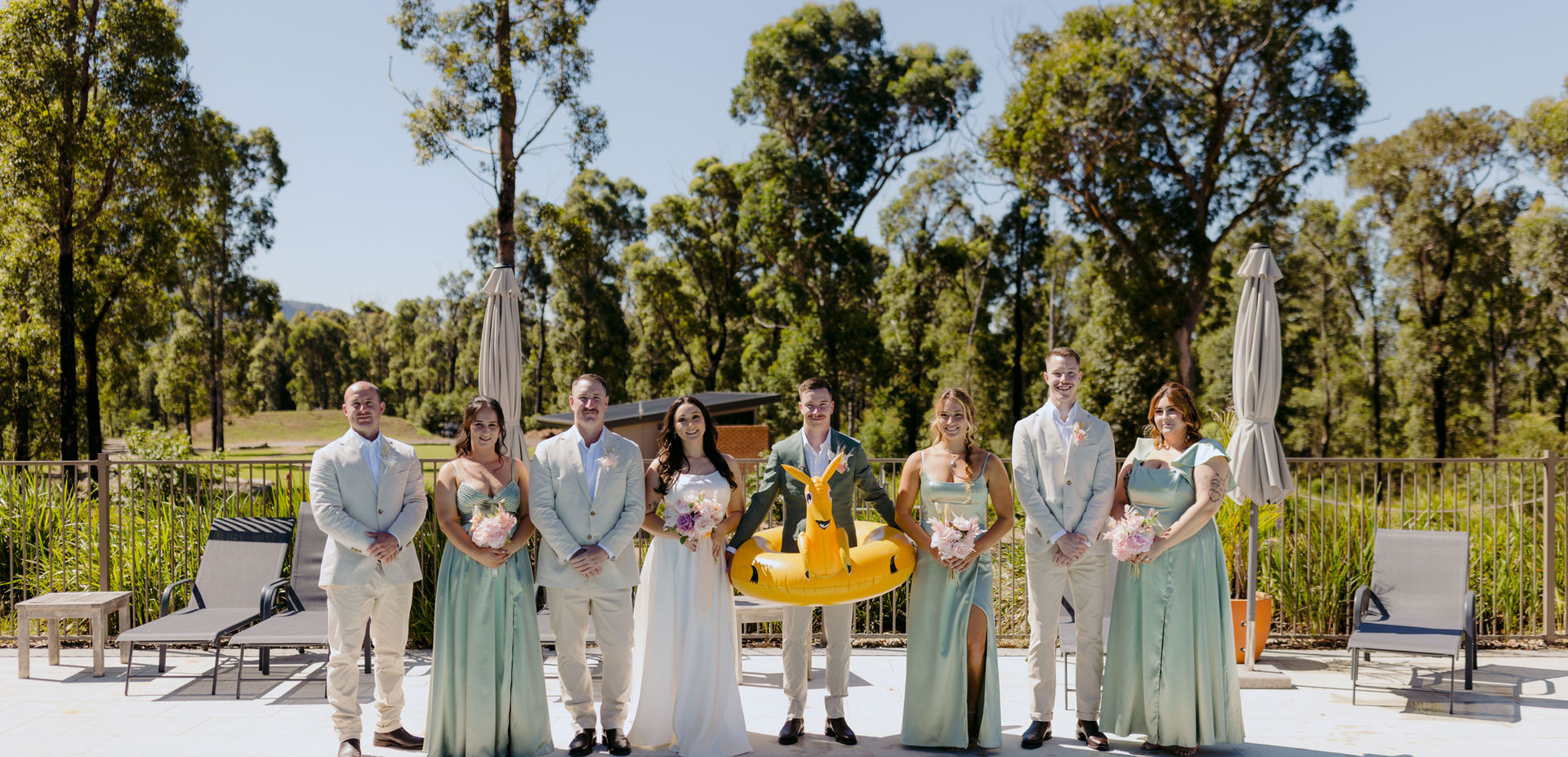 Bride, groom, bridesmaids, and groomsmen posing by pool with kangaroo float at KVBR.