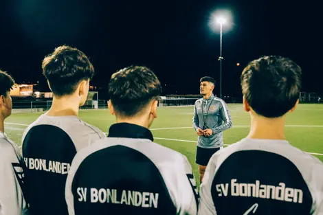 Athletiktrainer steht vor versammelter Mannschaft und spricht mit den Spielern.