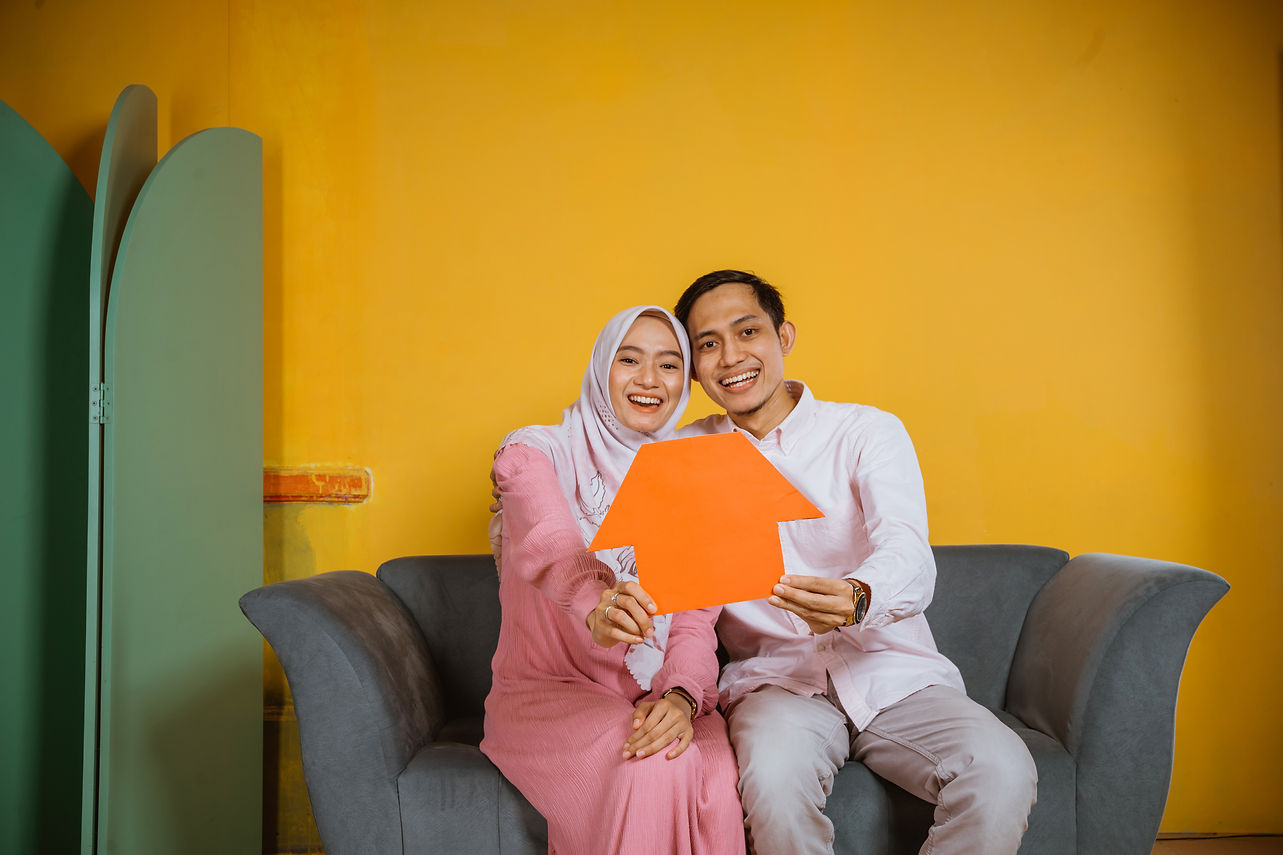 asian-muslim-man-woman-laugh-while-showing-house-shaped-paper-while-sitting-sofa.jpg