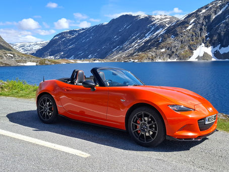 MX-5 car on a road in front of a lake and mountains