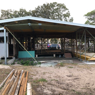 View of the roof line of a house under construction, with leftover wooden planks and an exposed interior. The additional room and suspended floor are visible, with no walls or deck yet.