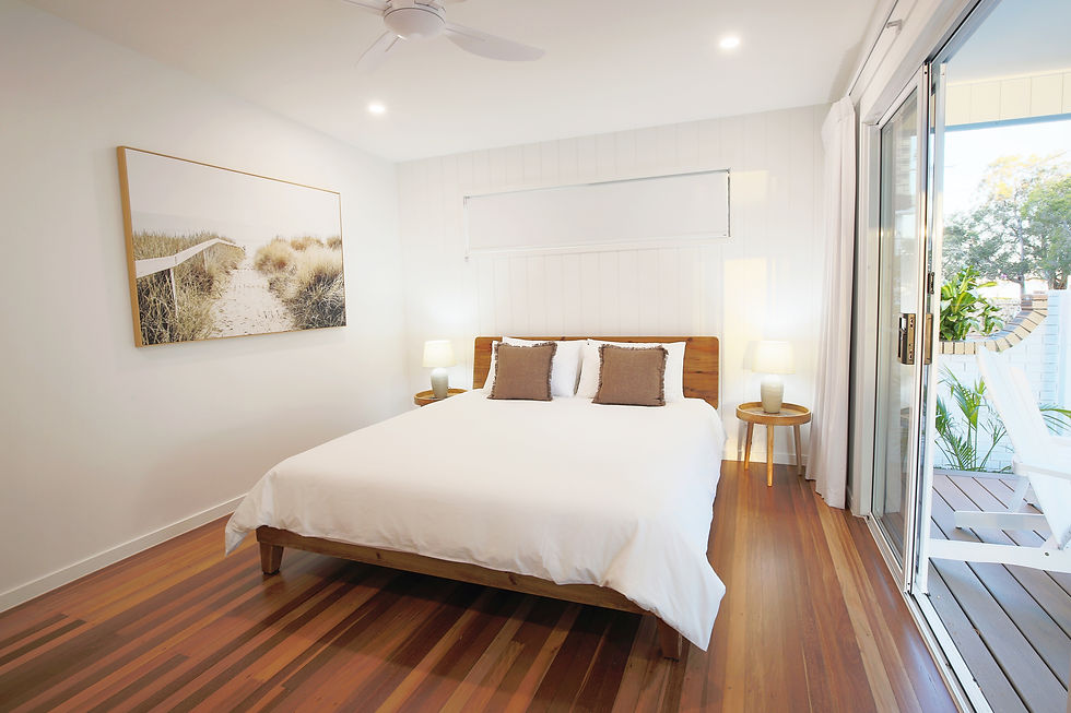 Master bedroom at Sylvan Beach House with white linen, coastal artwork, and glass doors.