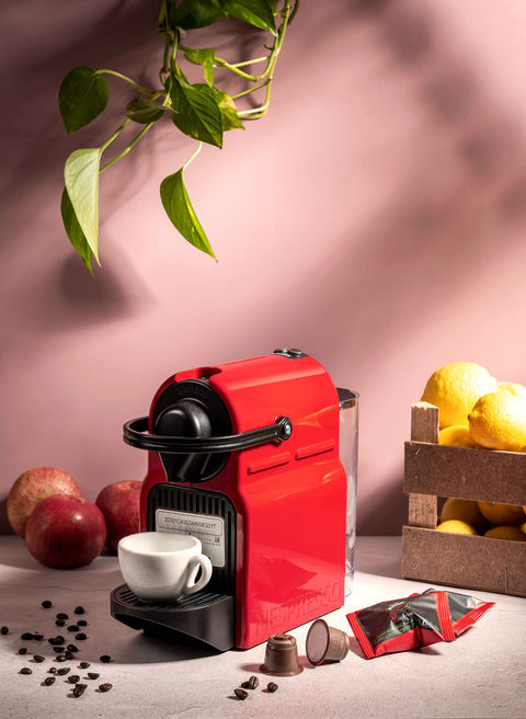 Macchina da caffè Nespresso rossa in still life contemporaneo con tazzina, capsule e limoni, fotografia di prodotto e lifestyle dal tono caldo e naturale.
