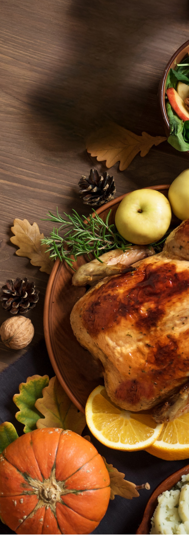 Roasted turkey on a rustic table with apples, rosemary, pumpkins, pinecones, and autumn leaves, creating a warm Thanksgiving feel