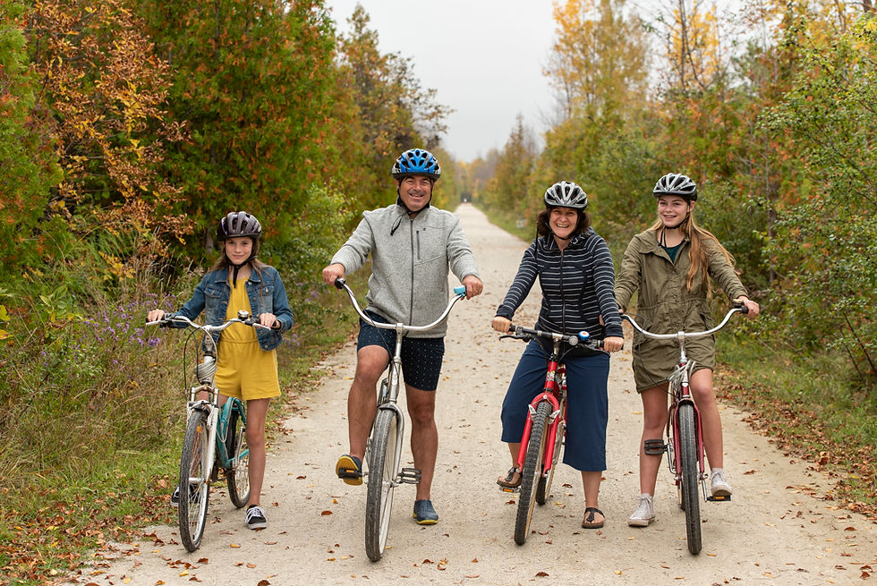 Family of four wearing helmets smiles while riding bicycles on a tree-lined autumn trail.