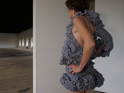 Robe crochetée aux doigts. Physionomie organique. Ruban jersey rayée blanc et bleu. Portée sur un corps, vu de profil. Un bras dénudé, l'autre bras avec une manche.