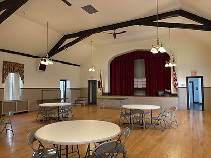 The empty Parish Hall with round tables and a stage in the background with a red curtain