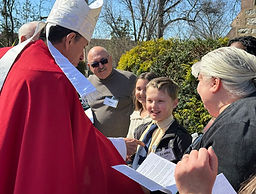 The Bishop of the Episcopal church blessing a young person while onlookers gather around smiling