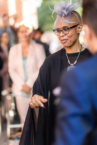 Freie Rednerin mit Brille und Fascinator bei Hochzeitszeremonie im Freien. A freelance speaker with glasses and beautiful headress at an outdoor ceremony.