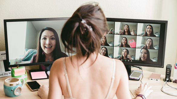 The back of a frazzled looking woman wearing a bra sitting in front of two computer monitors filled with images of her face in different expressions