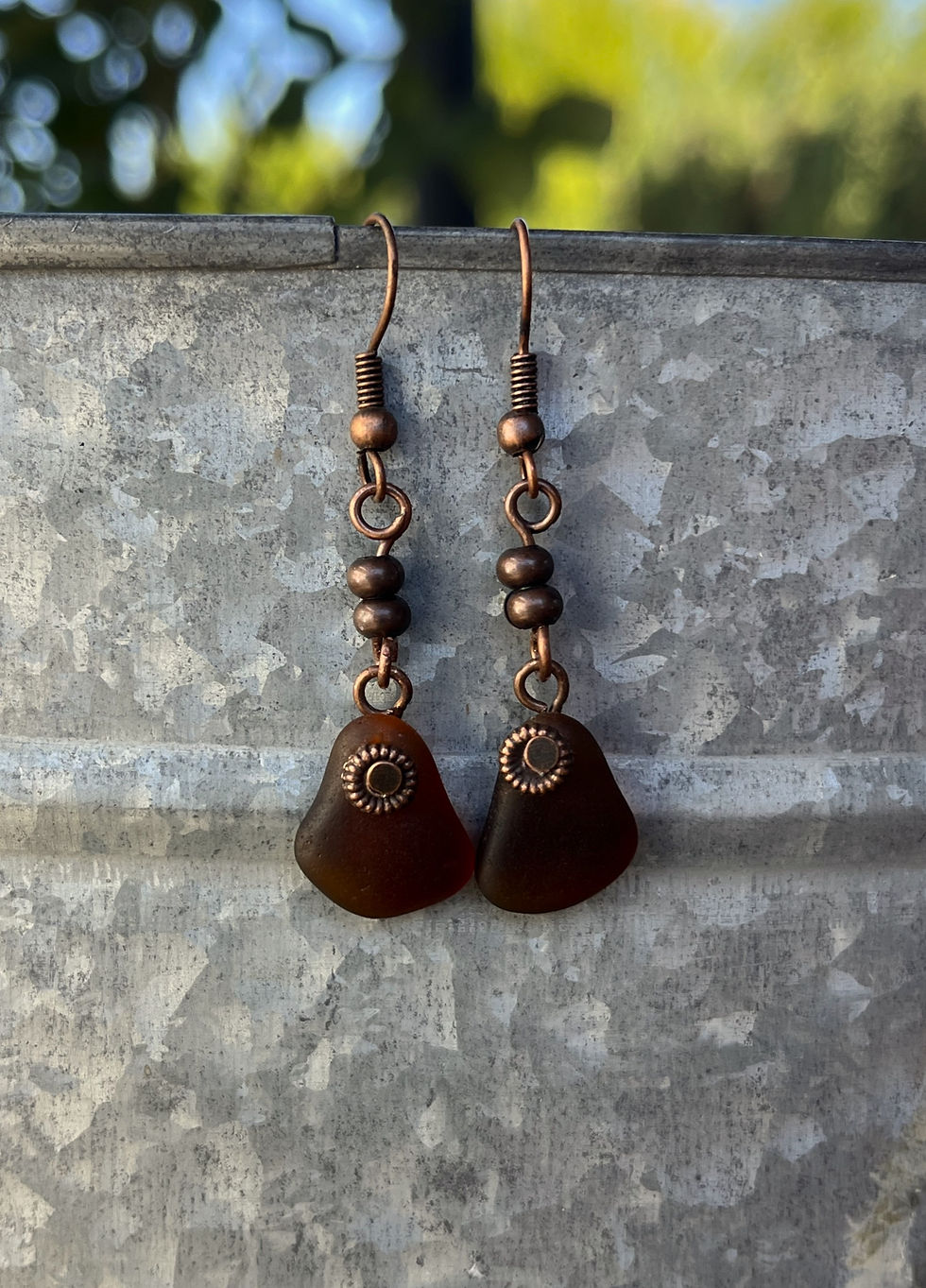 brown sea glass earrings made with antiqued copper beads and mermaid tears dangle from the edge of a can
