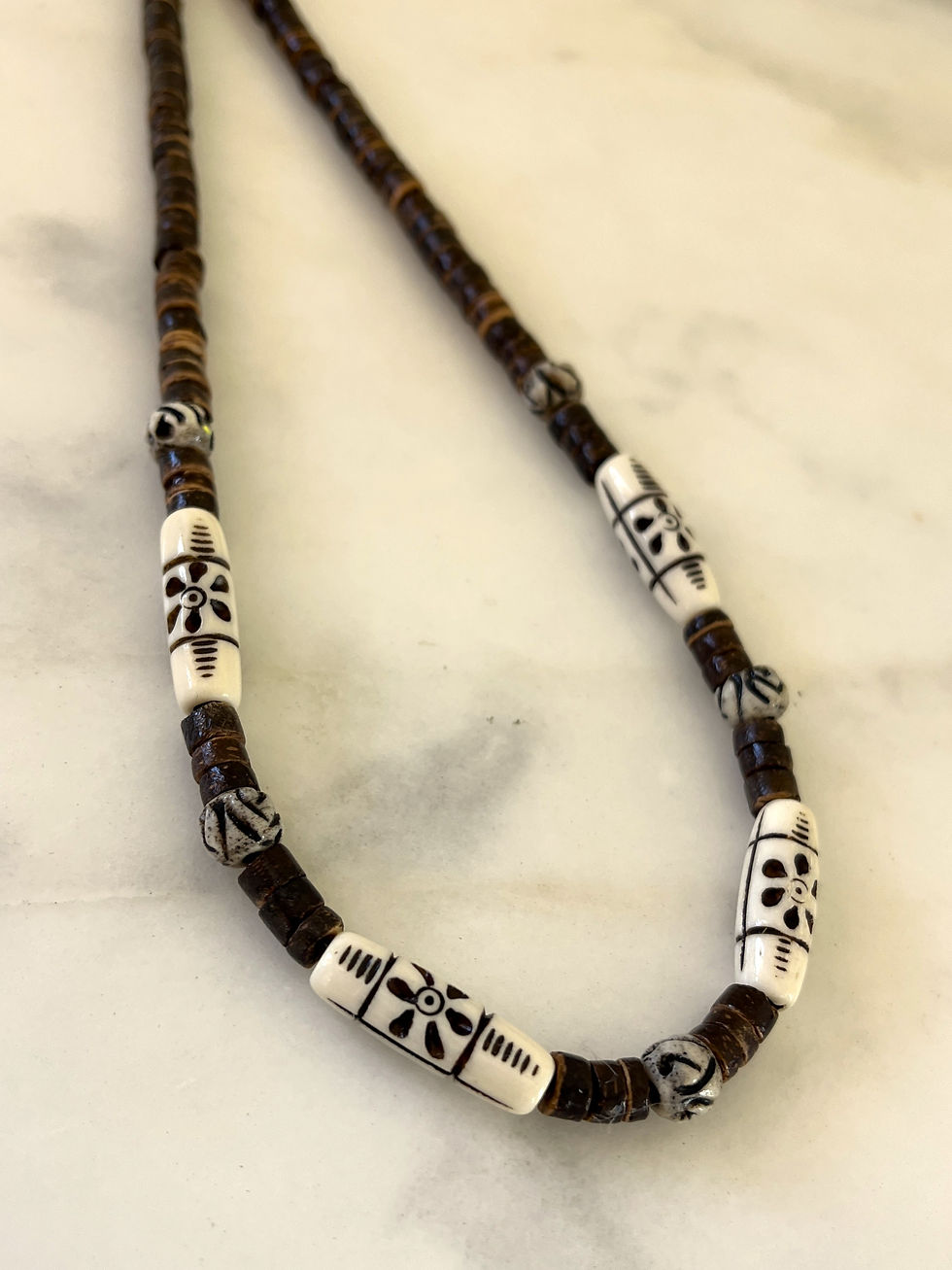 a thin surfer necklace beaded with brown coconut and white bone beads