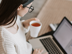 woman entrepreneur drinking coffee and working on a marketing audit of her business on a laptop in comfortable clothing