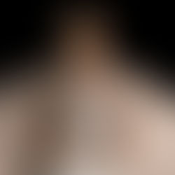 Woman in menopause considering hormone replacement therapy wearing a tan shirt and white jeans against a dark background