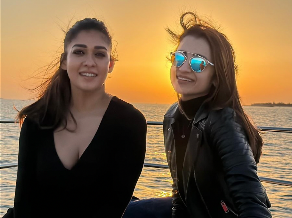 nayanthara in a low neck black top posing with trisha in a leather jacket in a yacht posing on the backdrop of a sunset