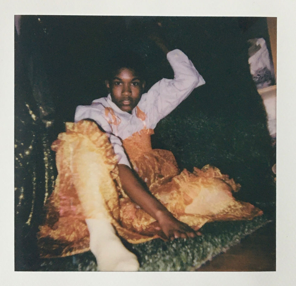 I am crouched in an orange tulle gown, with a white button up underneath, i look at the camera as though i am caught getting ready, there are no shoes on my stocking covered feet.