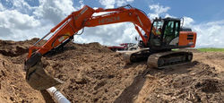 Excavator Laying Smaller Pipe surrounded by cleared land