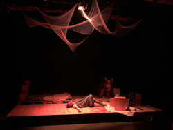 2023 Production: The Artist lays on the floor. The lighting is all red.