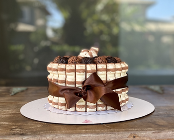 Bolo "Gostosura" decorado com Kinder Bueno e laço marrom, coberto com brigadeiros. Em uma mesa de madeira, fundo desfocado e ambiente acolhedor.